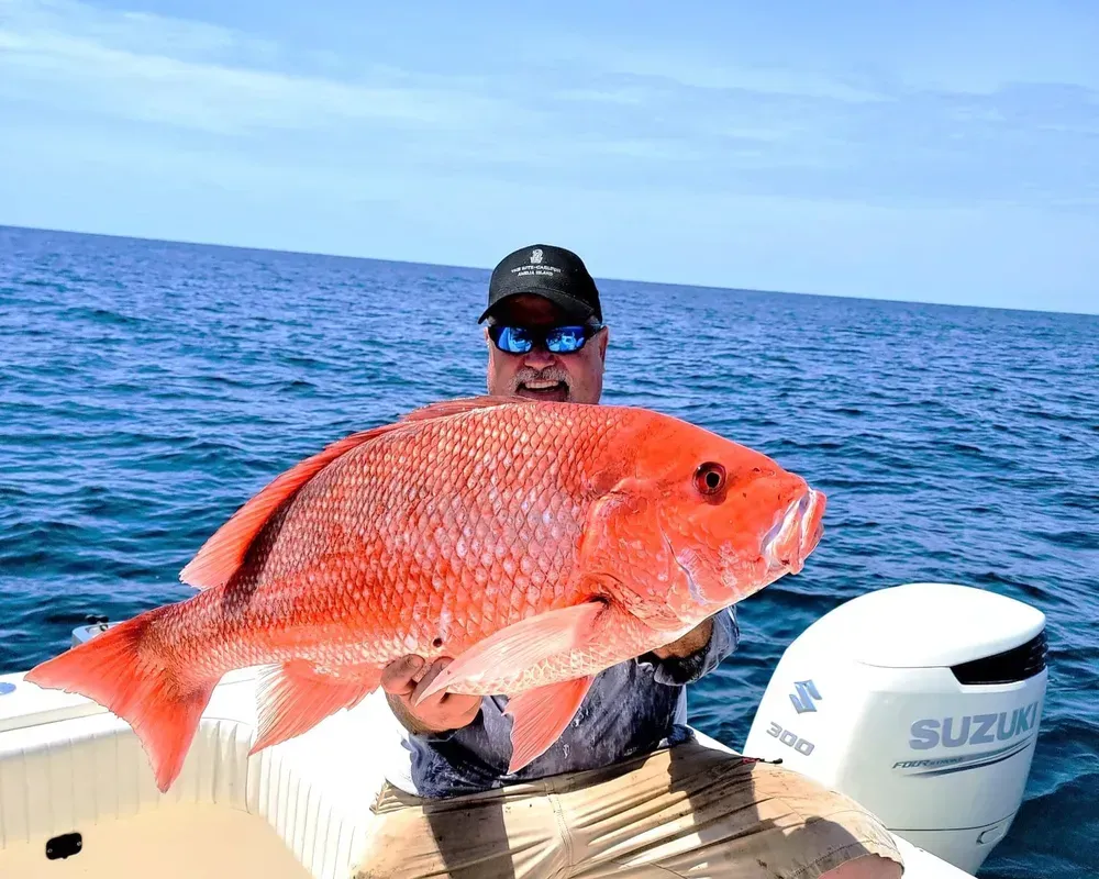 A man is holding a large red fish on a suzuki boat