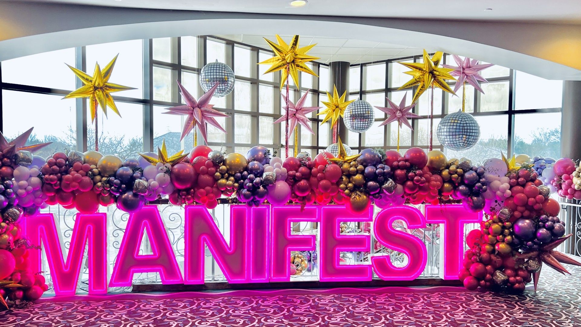 A glamorous event backdrop featuring bold, pink LED marquee letters spelling 