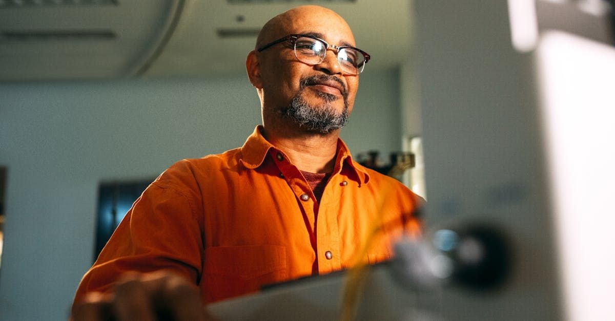 A man in an orange shirt and glasses is standing in front of a computer screen.