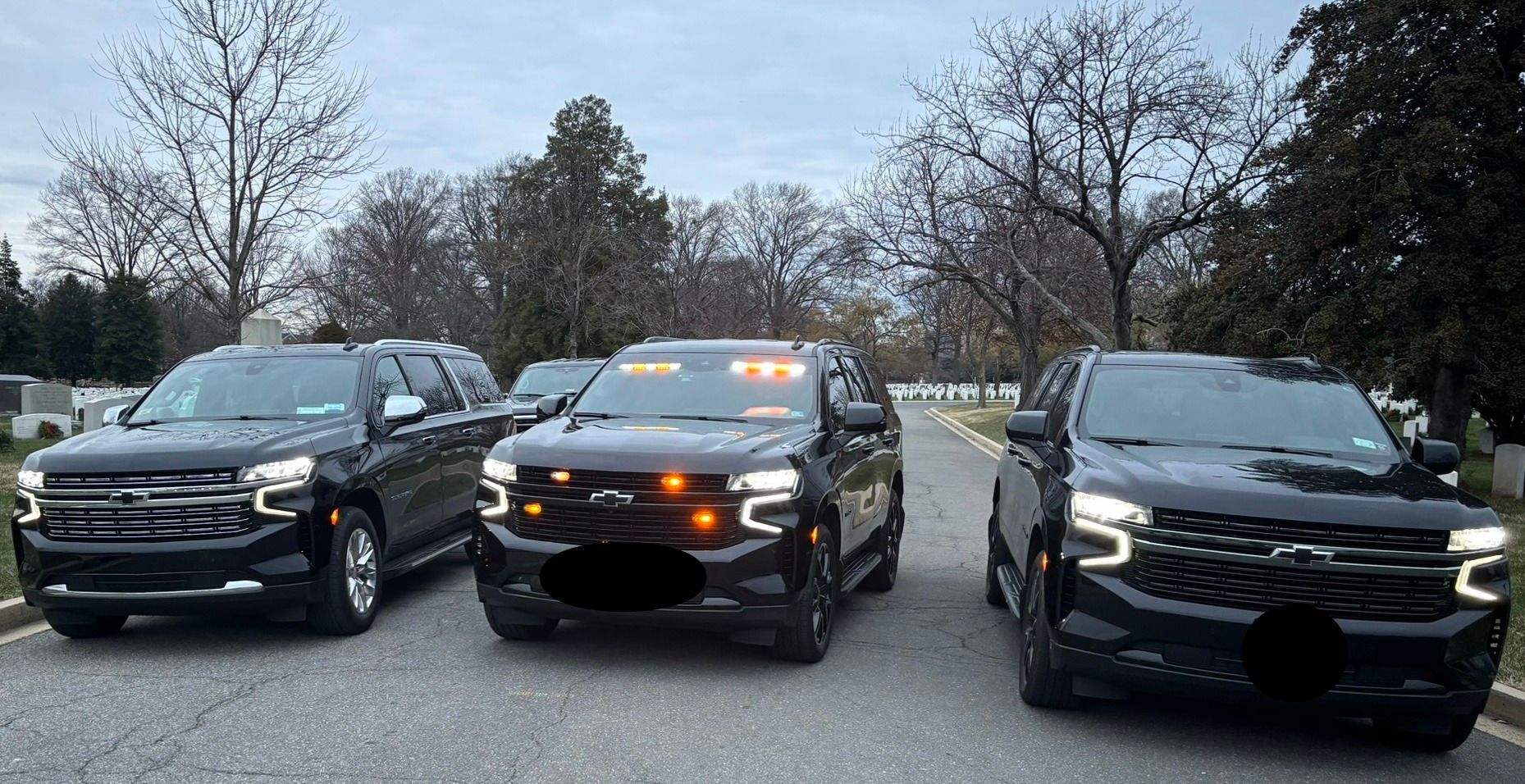 Three black SUVs parked on a road; an orange light bar is visible on the middle vehicle.