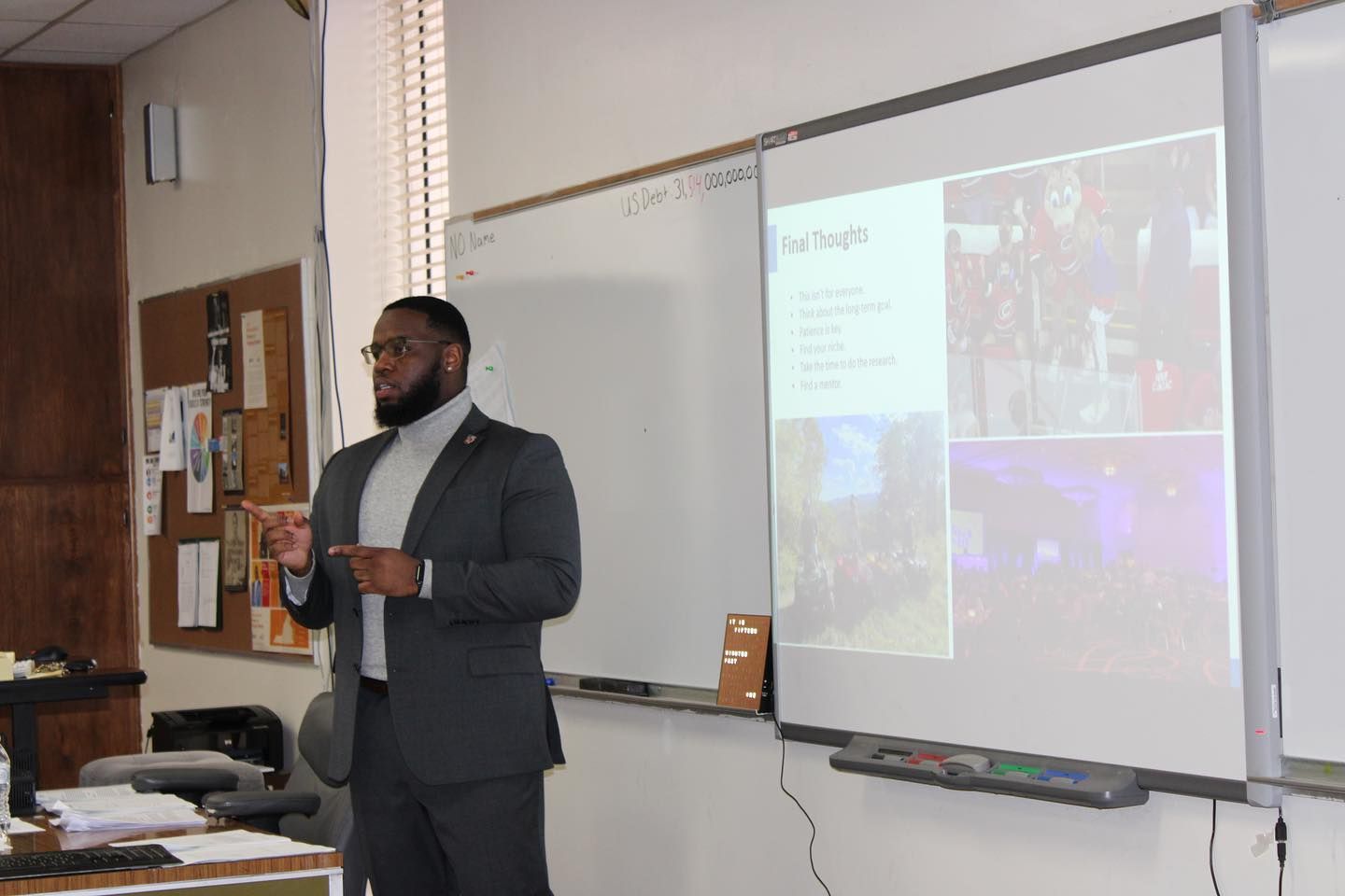 Man in suit presents at a whiteboard with images. Classroom setting.