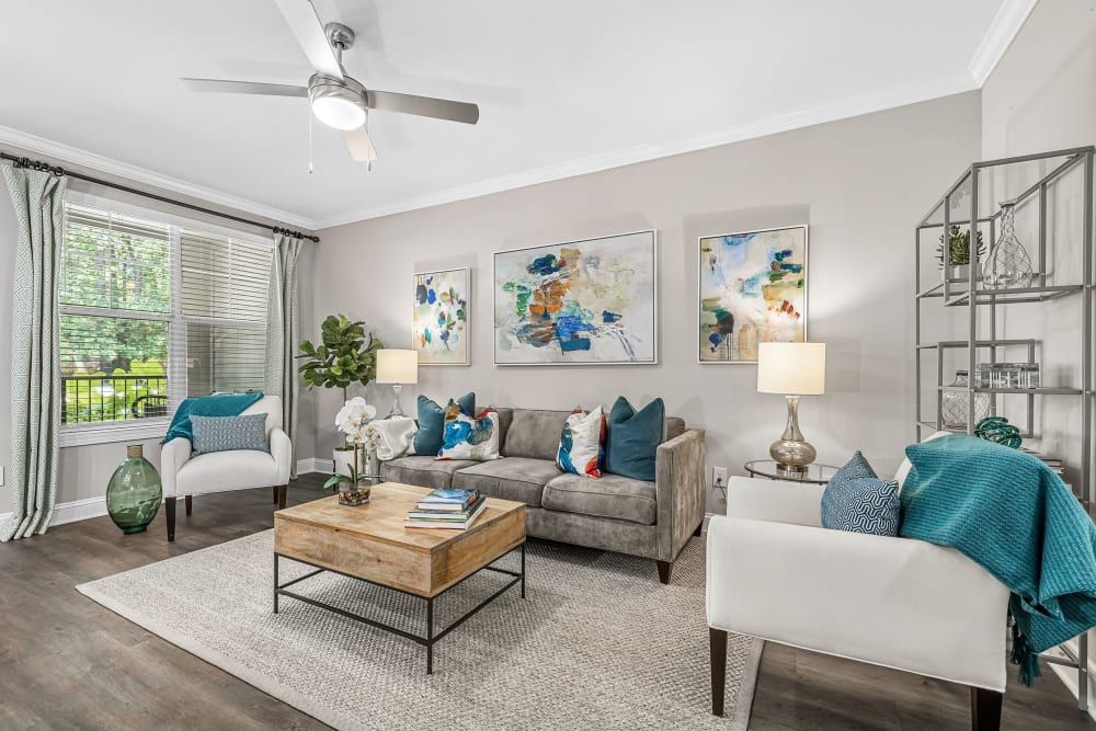 Stylish living room interior with natural light featuring gray and white furniture accented with blue throw pillows and blankets, abstract artwork on the walls, and a wooden coffee table on a textured area rug at Marq Perimeter in Atlanta, GA.