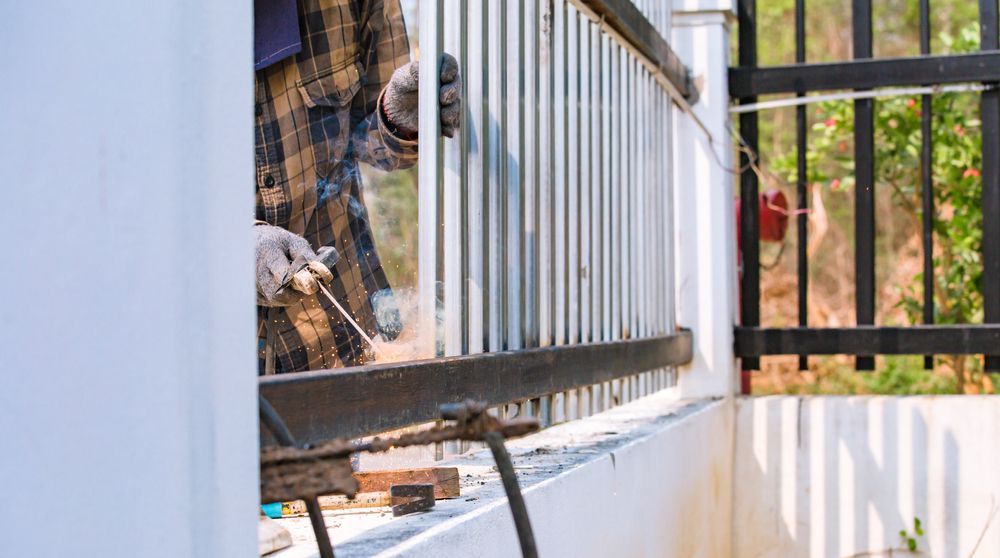 Person Welding Metal Railing on a White Balcony Next to a Black Fence — Busy Bees Blasting in Trinity Beach, QLD