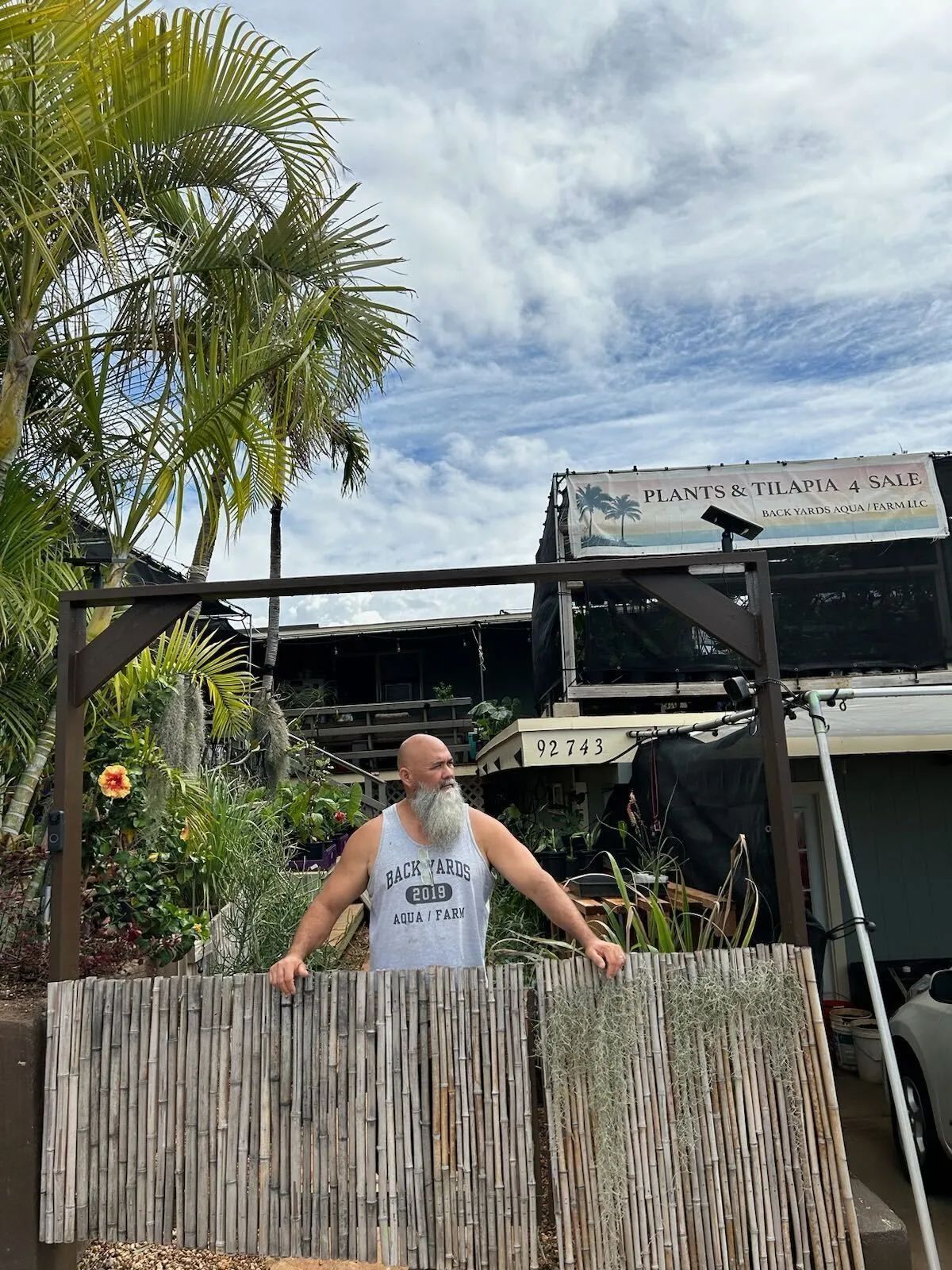 A man with a beard is standing next to a wooden fence.