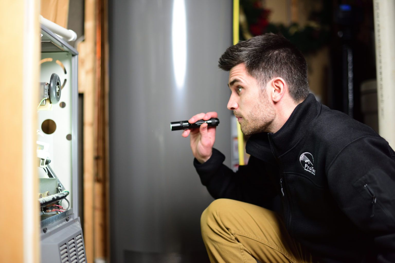 A man is looking at a water heater with a flashlight.
