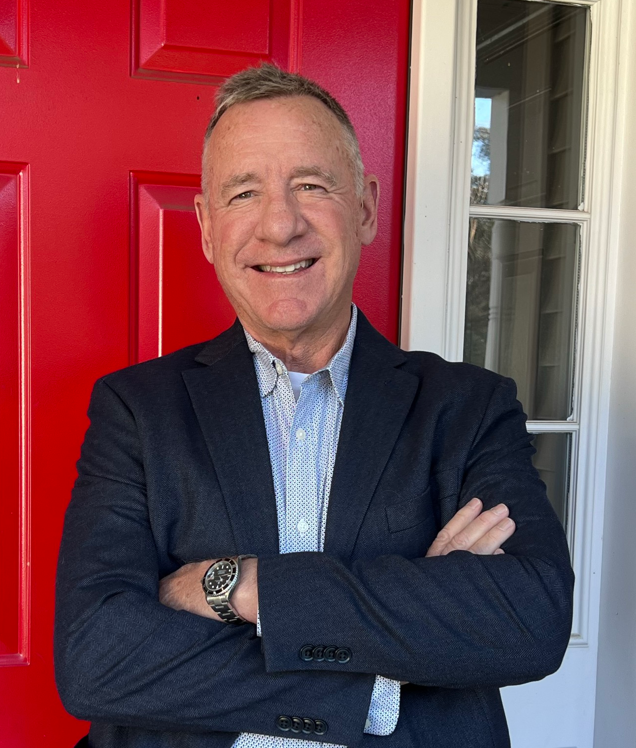 A man in a blue shirt is smiling in front of a red wall.