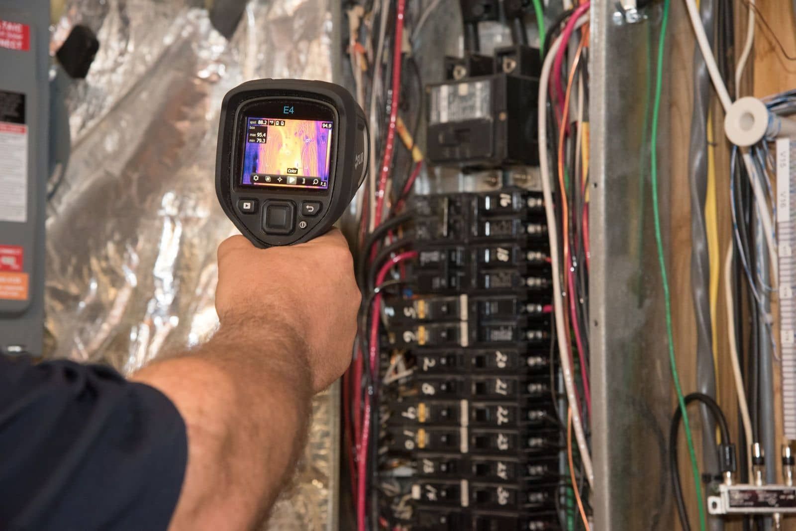 A man is holding a thermal camera over an electrical panel.