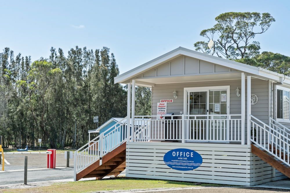 Office building with stairs, white railings, and a blue sign. Gray siding, surrounded by trees— SeaChange Parks Milton in Lake Conjola, NSW