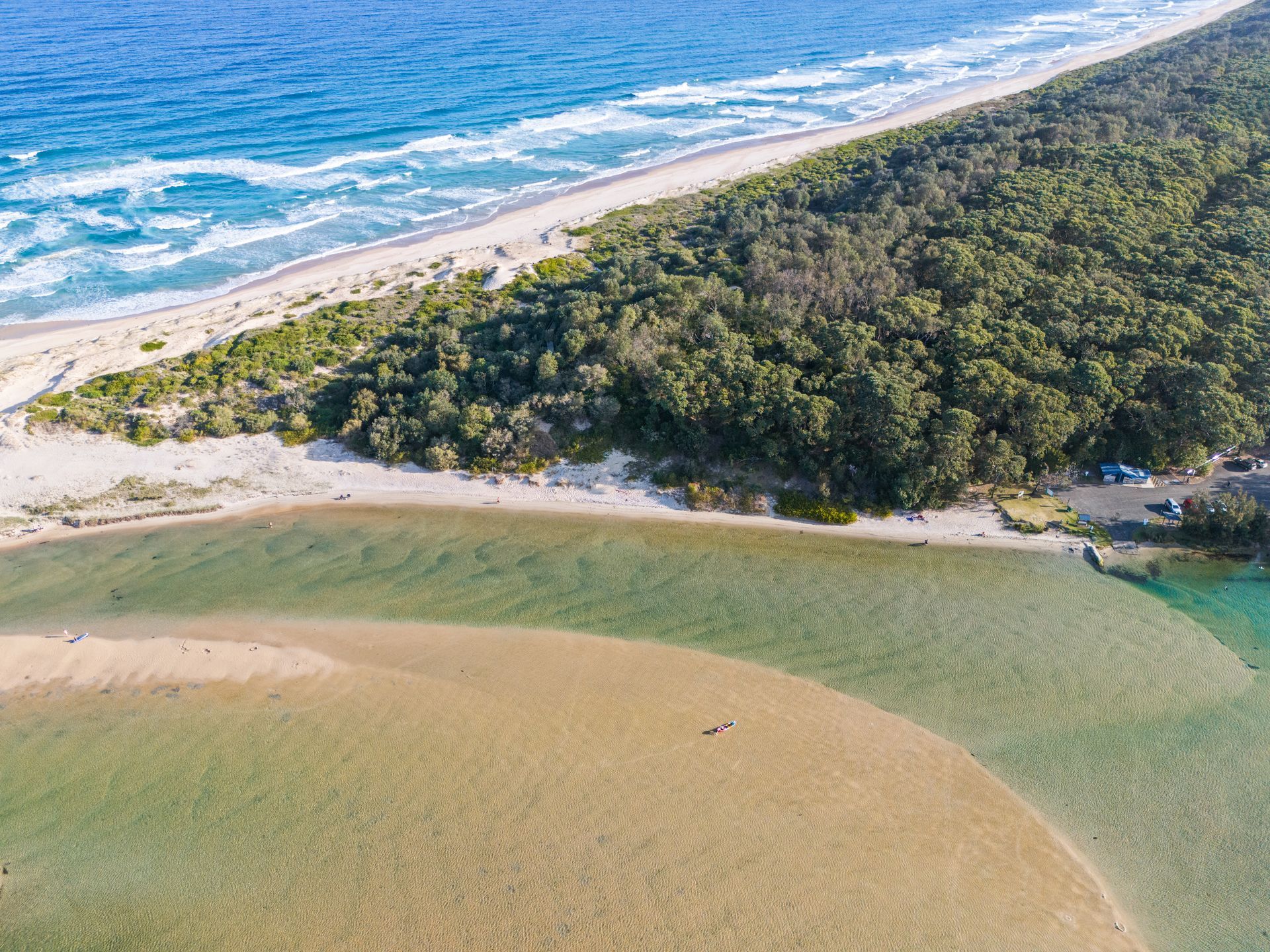 Lake scene: yellow kayaks, small island, building, grassy shore, and overcast sky — SeaChange Parks Milton in Lake Conjola, NSW