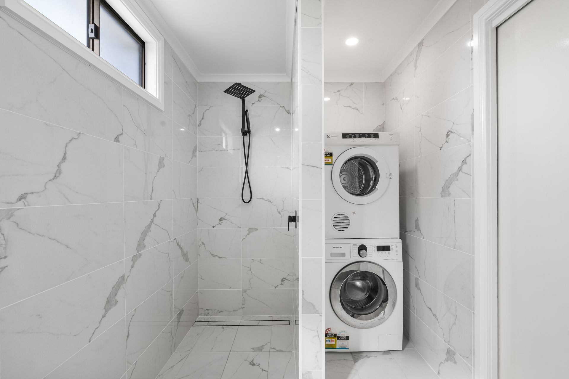 Bathroom with marble tile; shower and stacked washer/dryer are visible. Black showerhead, white appliances — SeaChange Parks Milton in Lake Conjola, NSW