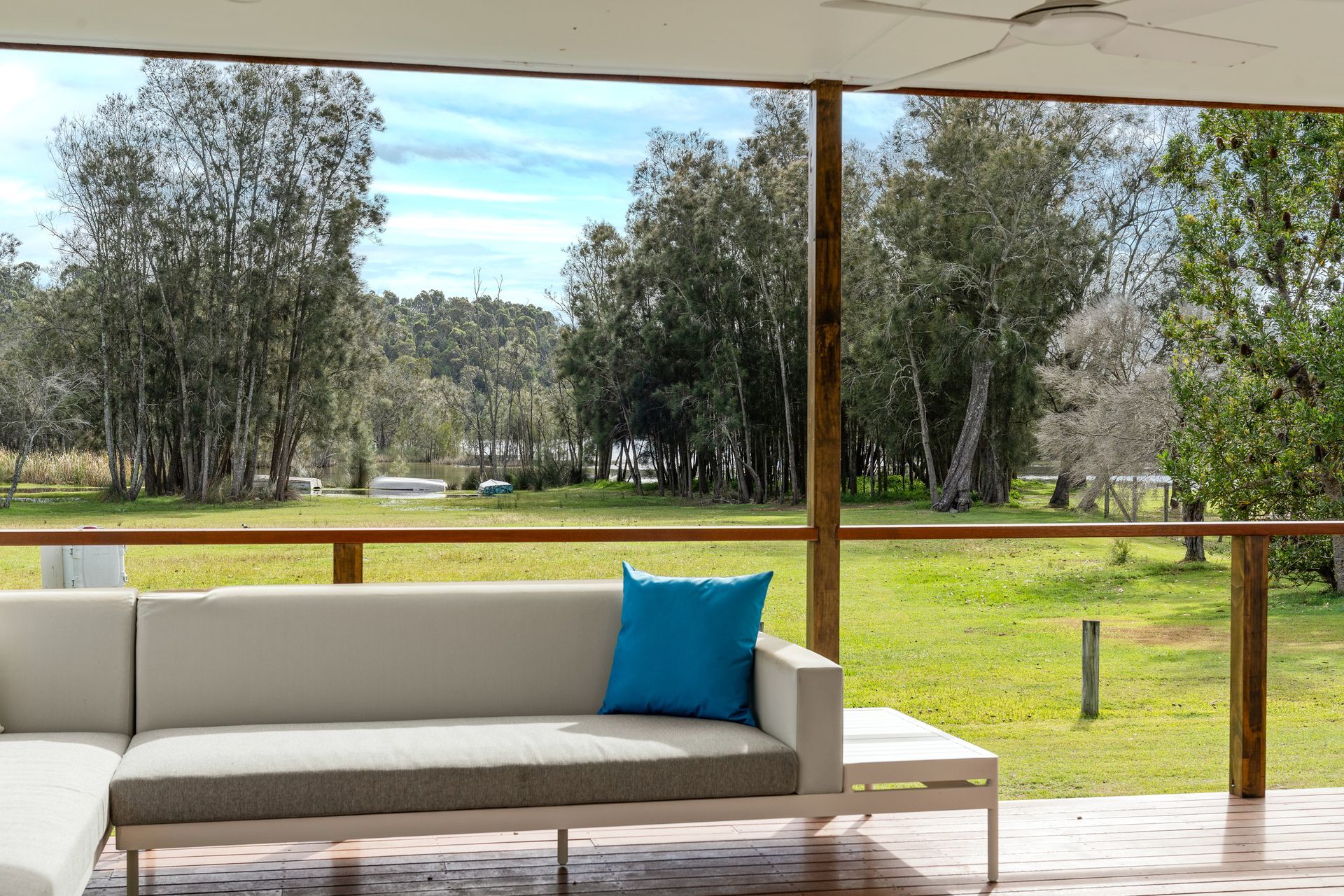 Outdoor seating area with a white couch and blue cushion overlooking a grassy field and trees— SeaChange Parks Milton in Lake Conjola, NSW