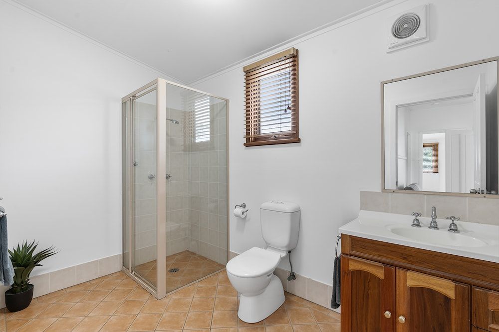 A bright bathroom featuring a walk-in glass shower, toilet, and vanity with a mirror and wooden cabinets. — SeaChange Parks Milton in Lake Conjola, NSW