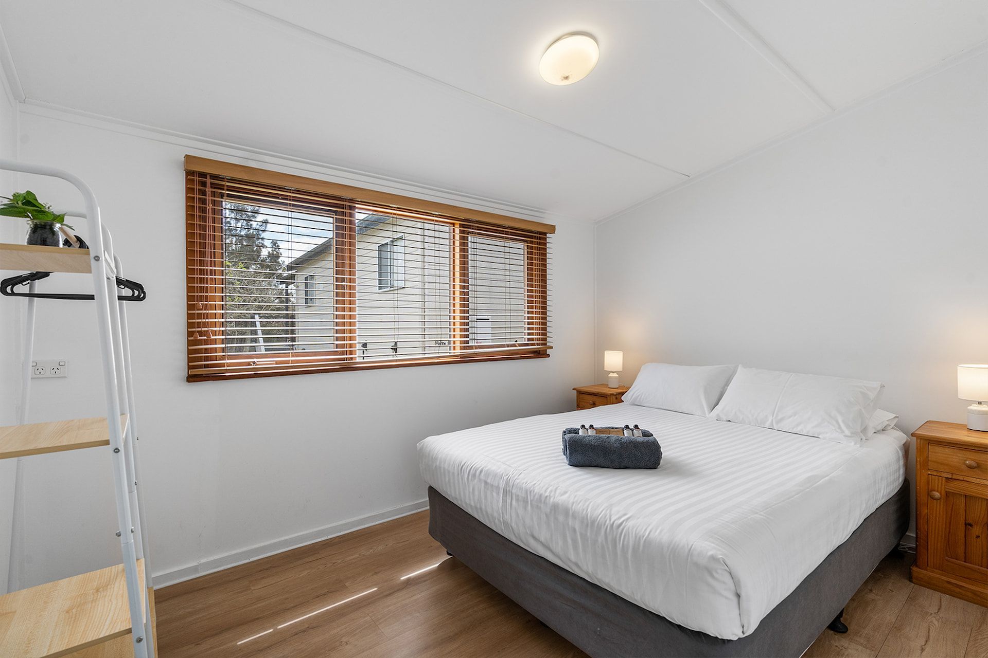 Bedroom with a double bed, wooden blinds, nightstands, and a shelving unit — SeaChange Parks Milton in Lake Conjola, NSW