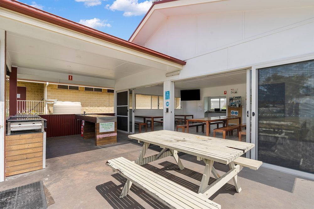 Outdoor Patio With Picnic Table, Grill, and Seating Area Under a White Roof — SeaChange Parks Milton in Lake Conjola, NSW