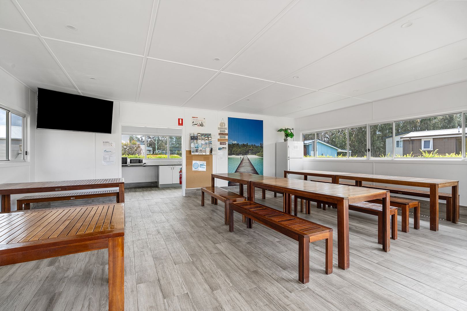 Interior of a dining hall with wooden tables, benches, and a large TV. Windows on one side — SeaChange Parks Milton in Lake Conjola, NSW