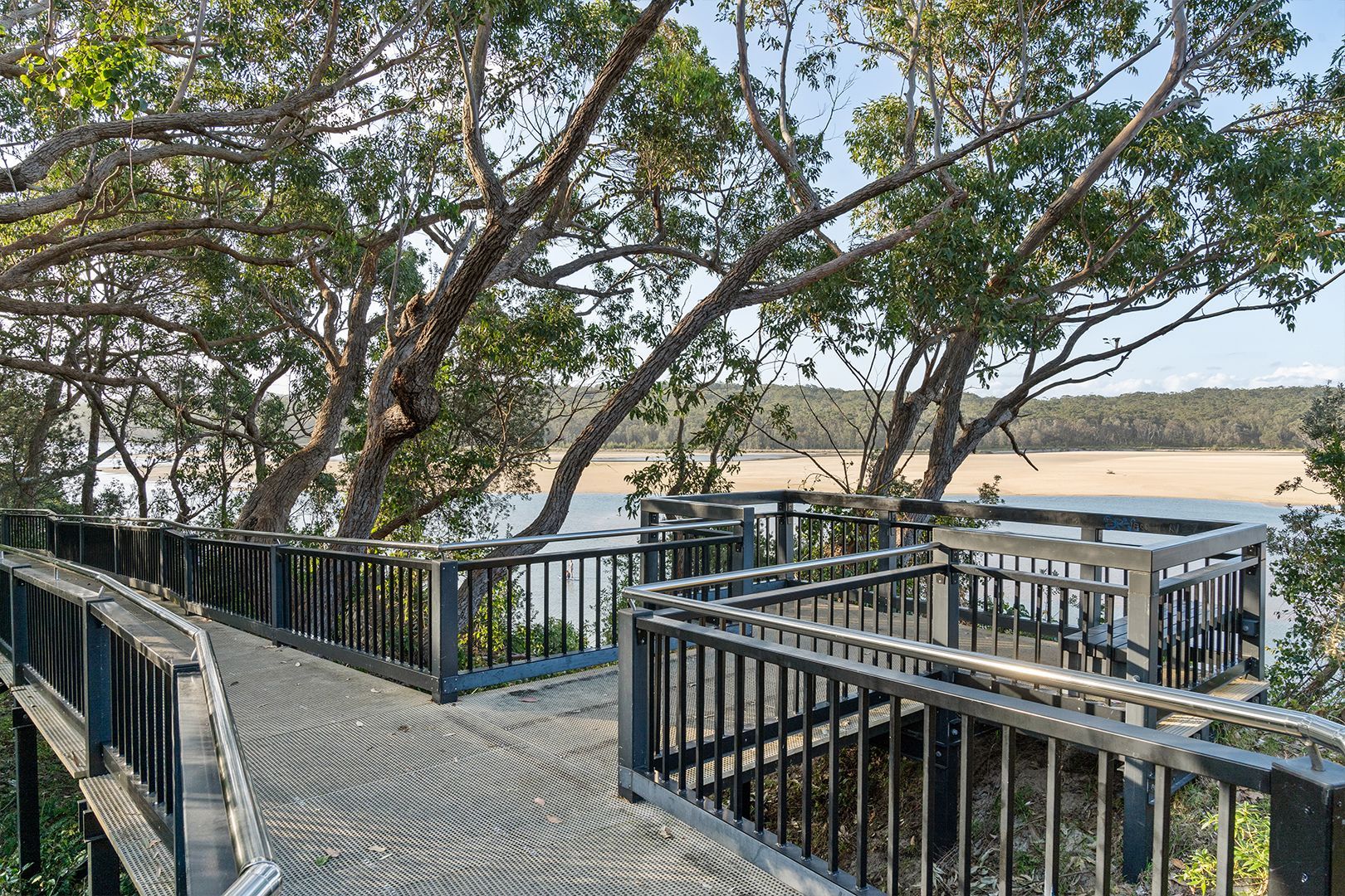 Elevated boardwalk with railings, overlooking water and trees on a sunny day — SeaChange Parks Milton in Lake Conjola, NSW