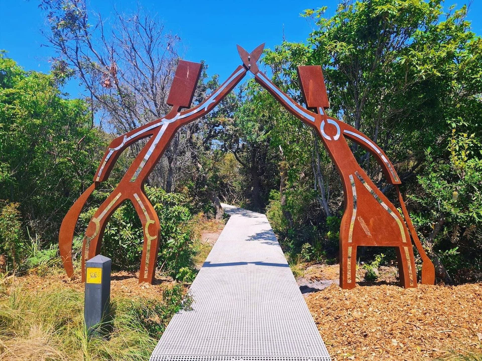 Metal sculpture archway over a boardwalk path surrounded by greenery — SeaChange Parks Milton in Lake Conjola, NSW