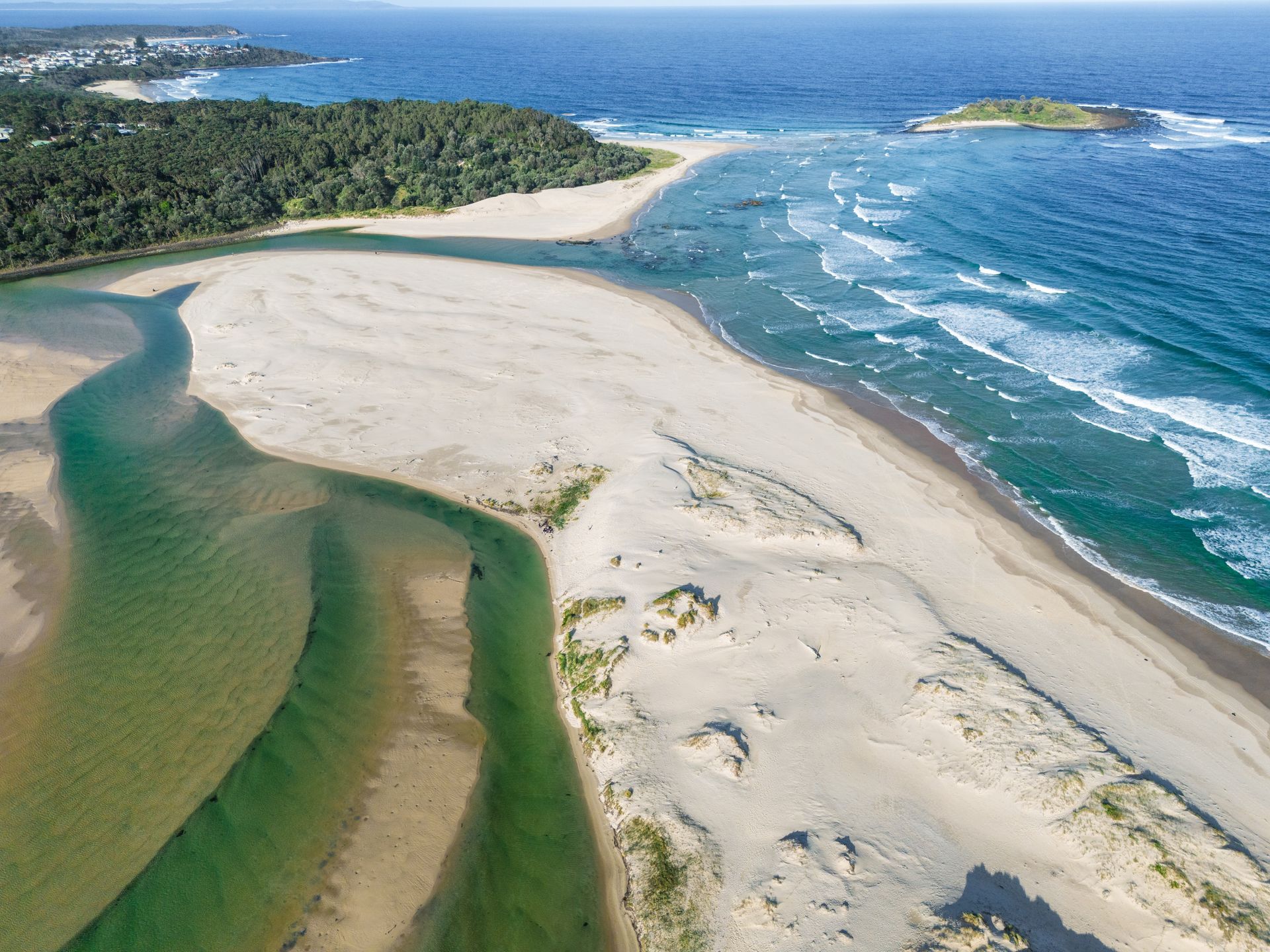An aerial view of a river mouth meeting the ocean, featuring a sandbar, lush green vegetation, and a small island offshore - SeaChange Parks Milton in Milton, NSW