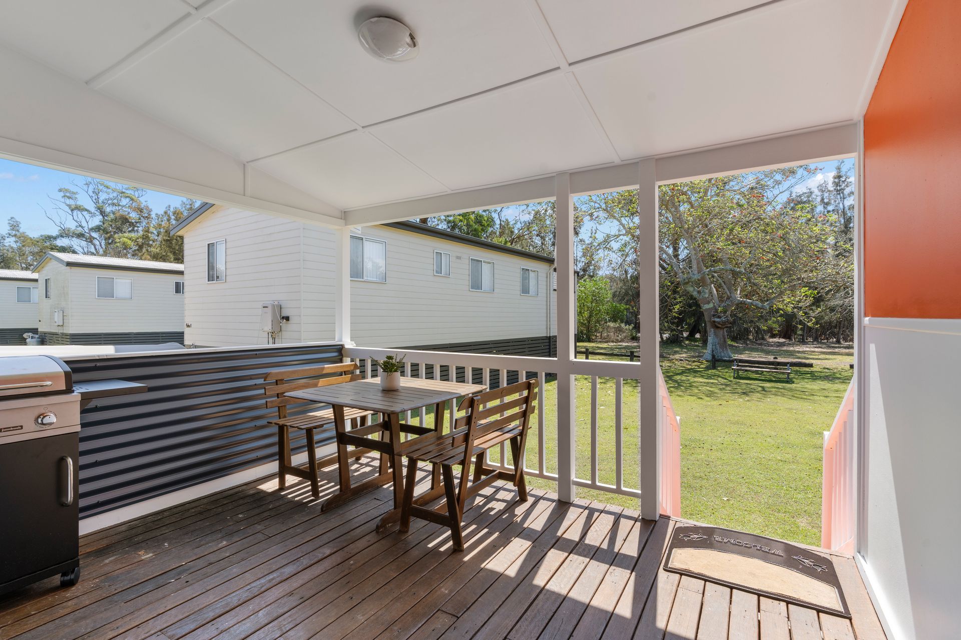 Outdoor patio with table, chairs, and grill; cabins in background — SeaChange Parks Milton in Lake Conjola, NSW