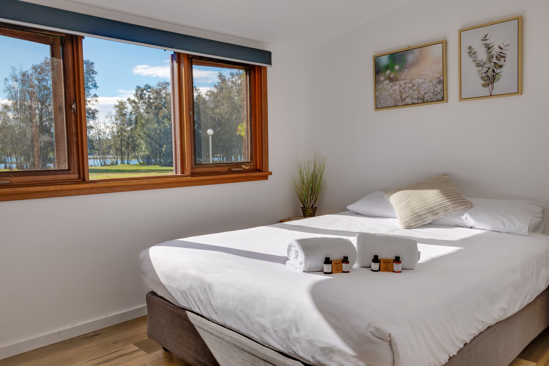 Bedroom with double bed, large windows with a view of a park, and two framed pictures on the wall — SeaChange Parks Milton in Lake Conjola, NSW