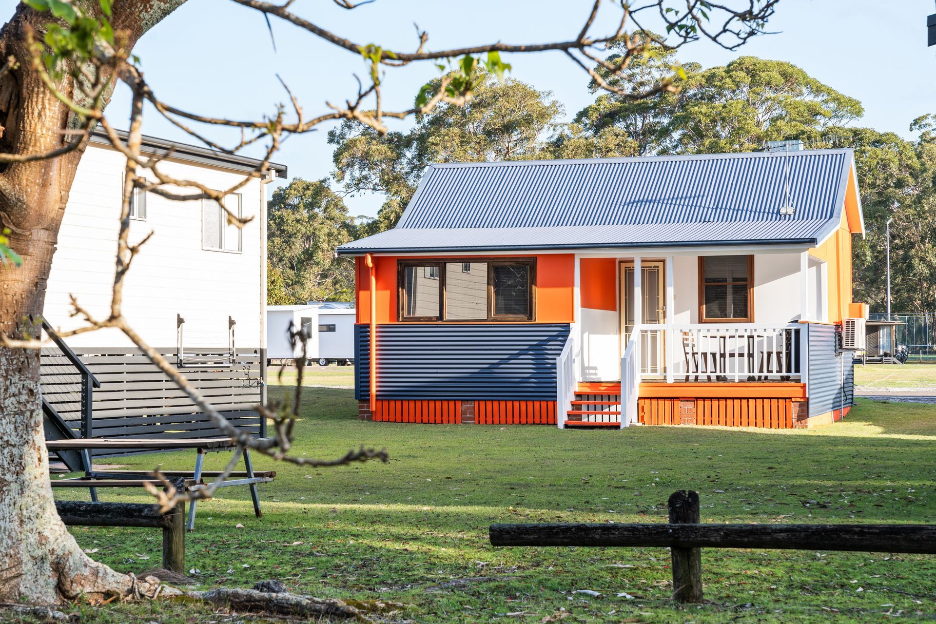 Small colourful cottage with porch and blue roof in a grassy park — SeaChange Parks Milton in Lake Conjola, NSW