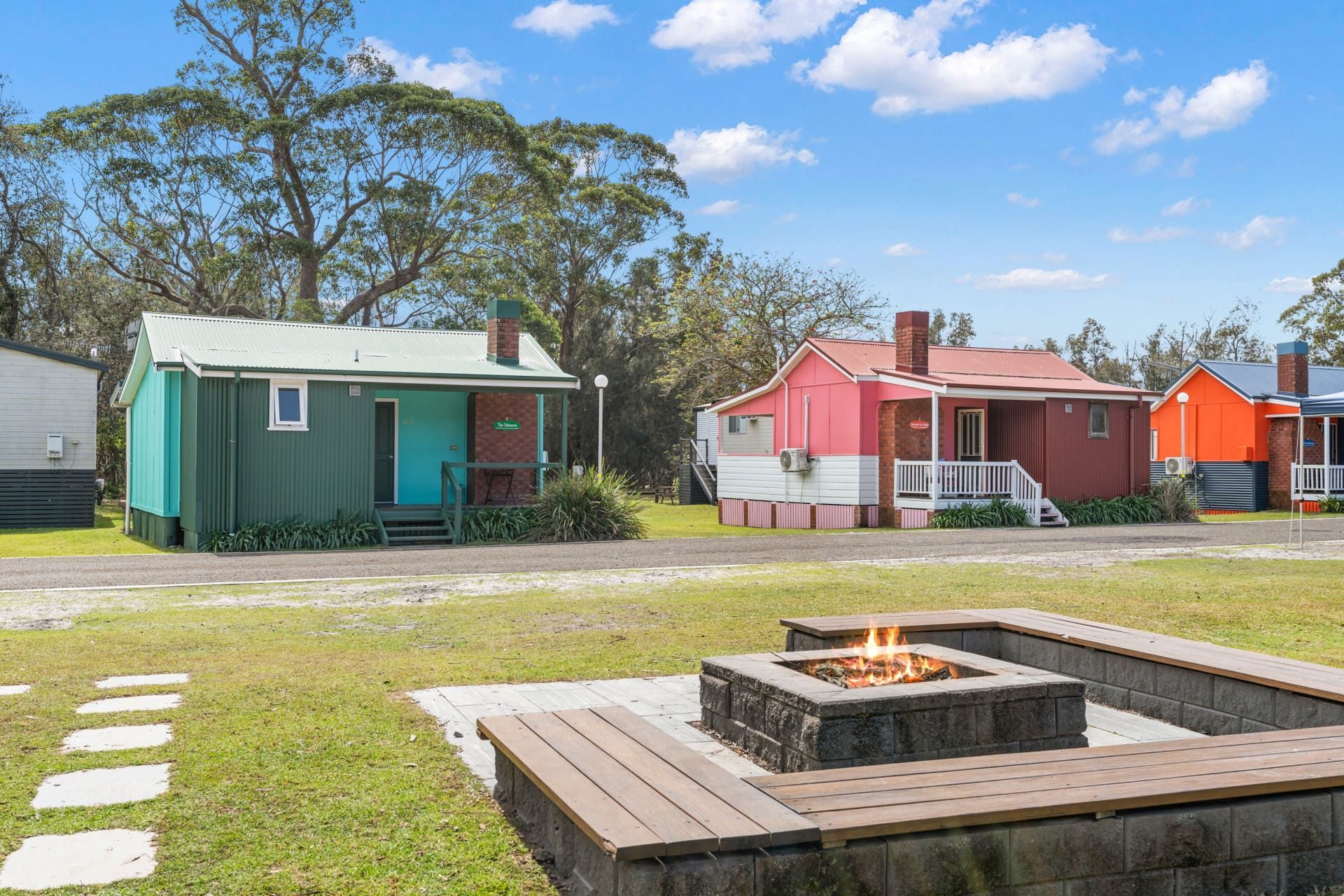 Colourful cabins with a fire pit in a grassy area, under a blue sky — SeaChange Parks Milton in Lake Conjola, NSW
