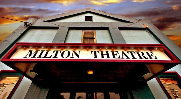 The illuminated Hilton Theatre entrance at night, featuring a marquee sign and two display posters on a cream facade — SeaChange Parks Milton in Milton, NSW