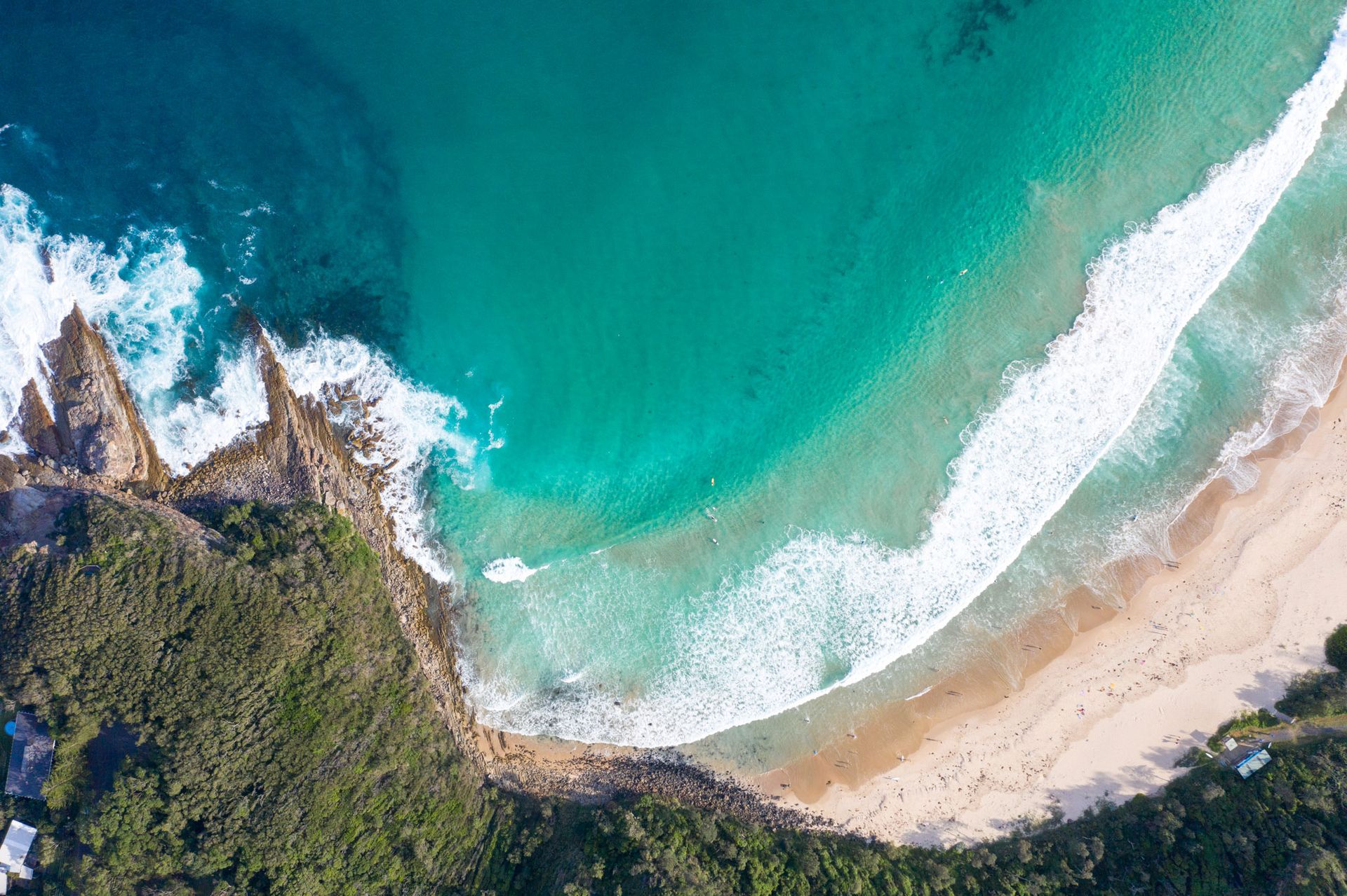 Aerial view of a turquoise ocean coastline with crashing white waves meeting a sandy beach beside green forest cliffs — SeaChange Parks Milton in Milton, NSW
