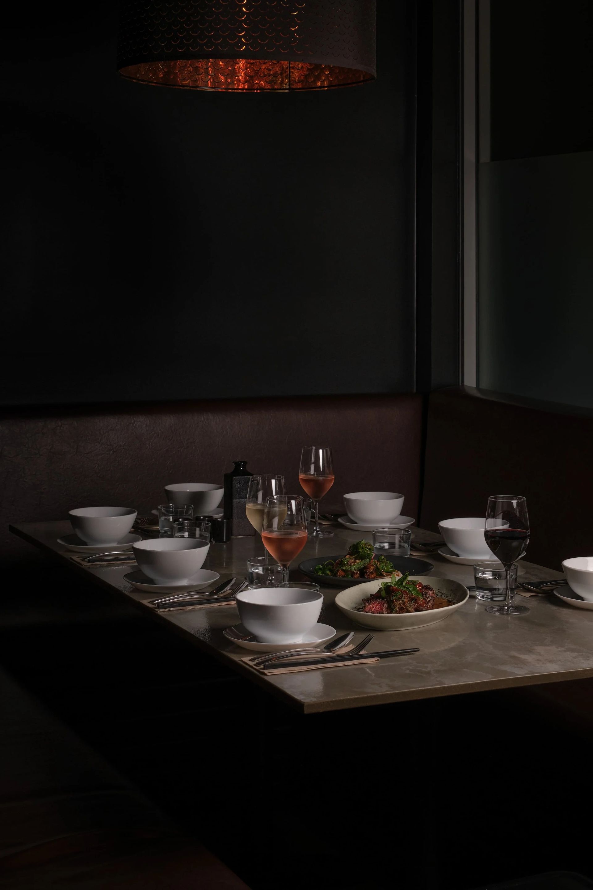 A dimly lit table set for a meal in a dark, intimate restaurant booth, featuring white bowls and wine glasses — SeaChange Parks Milton in Milton, NSW