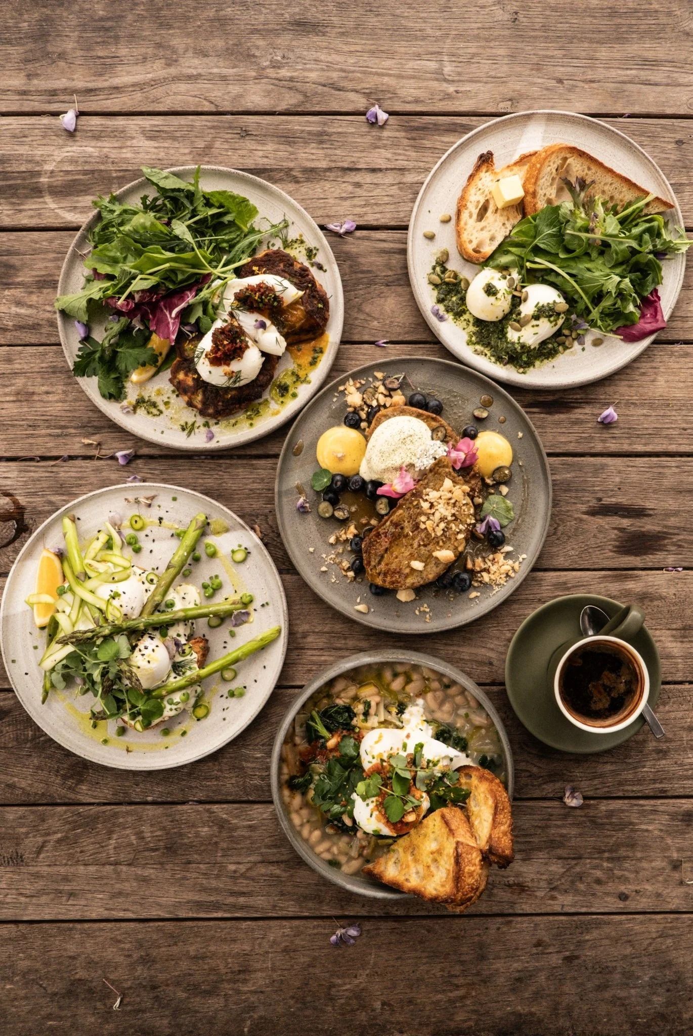 A top-down view of five diverse brunch dishes and a cup of coffee arranged on a rustic wooden table — SeaChange Parks Milton in Milton, NSW