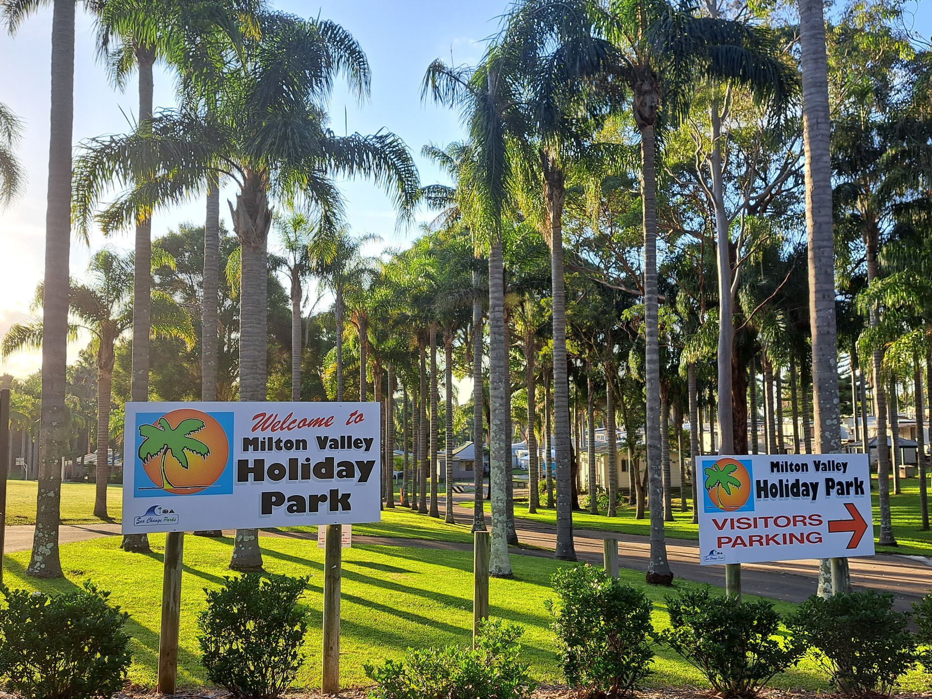 A sign for the Mission Valley Holiday Park with palm trees in the background on a sunny day  — SeaChange Parks Milton in Milton, NSW