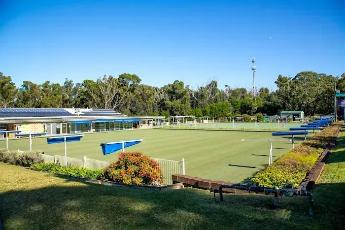 A bowling green with a clubhouse featuring solar panels, set against a backdrop of trees under a clear blue sky — SeaChange Parks Milton in Milton, NSW