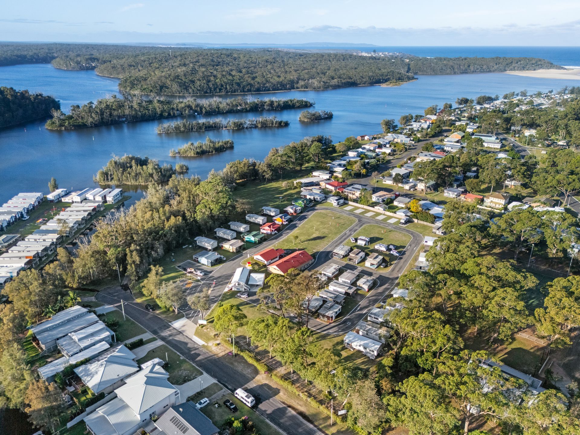 Aerial view of a coastal town with houses, a campground, and water, under a sunny sky — SeaChange Parks Milton in Milton, NSW