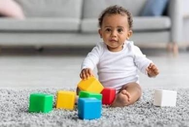 Baby playing with colorful building blocks on a carpeted floor.