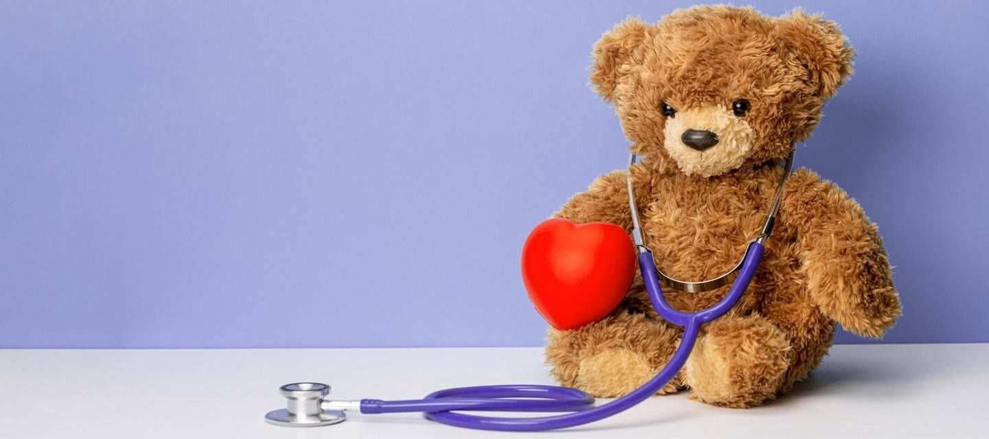 Brown teddy bear with a red heart, stethoscope. Purple background.