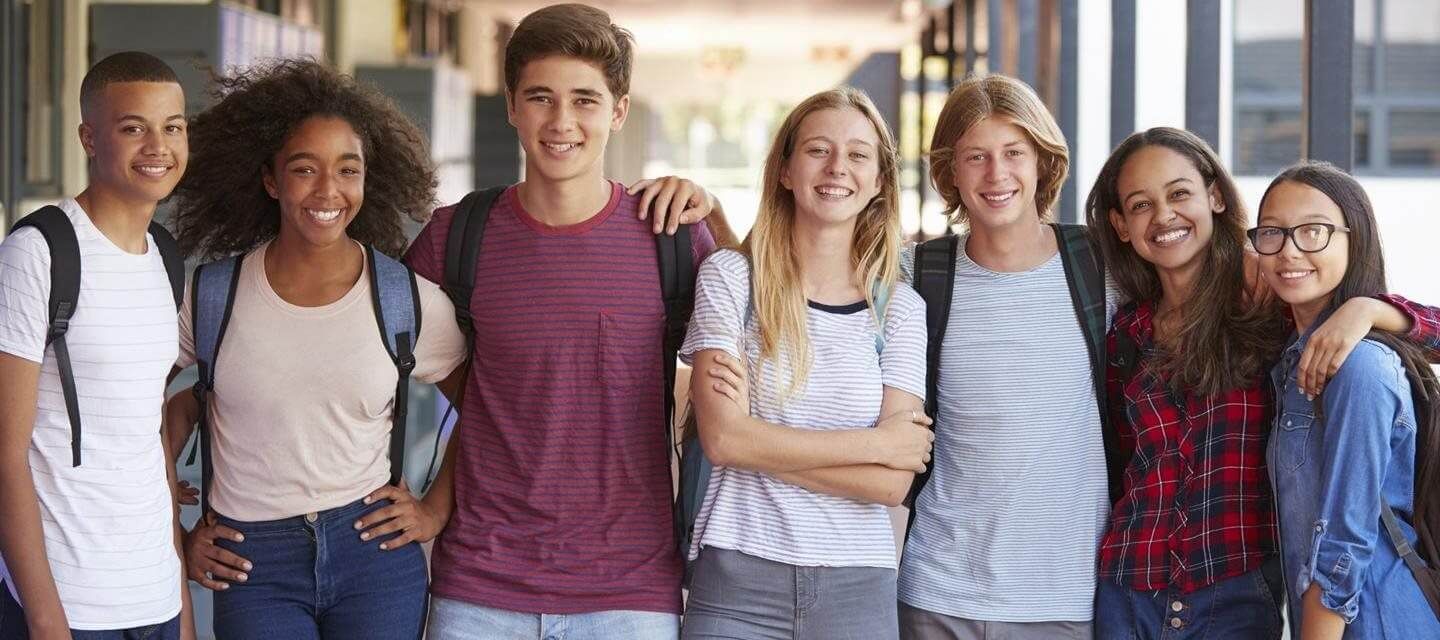 Group of smiling teens with backpacks posing outdoors.