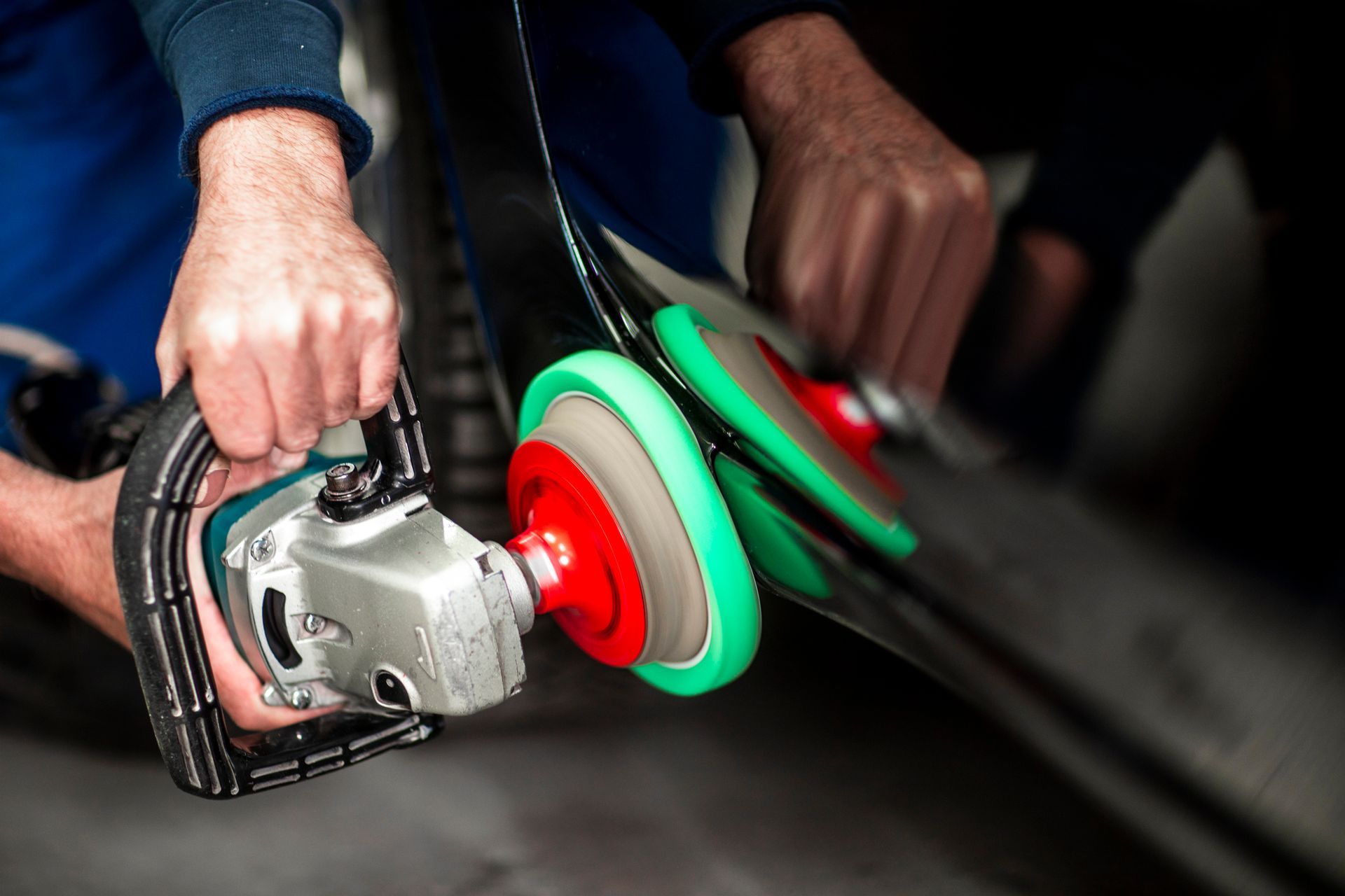 Close-up of hands holding a portable handheld polisher on the surface of a black car.