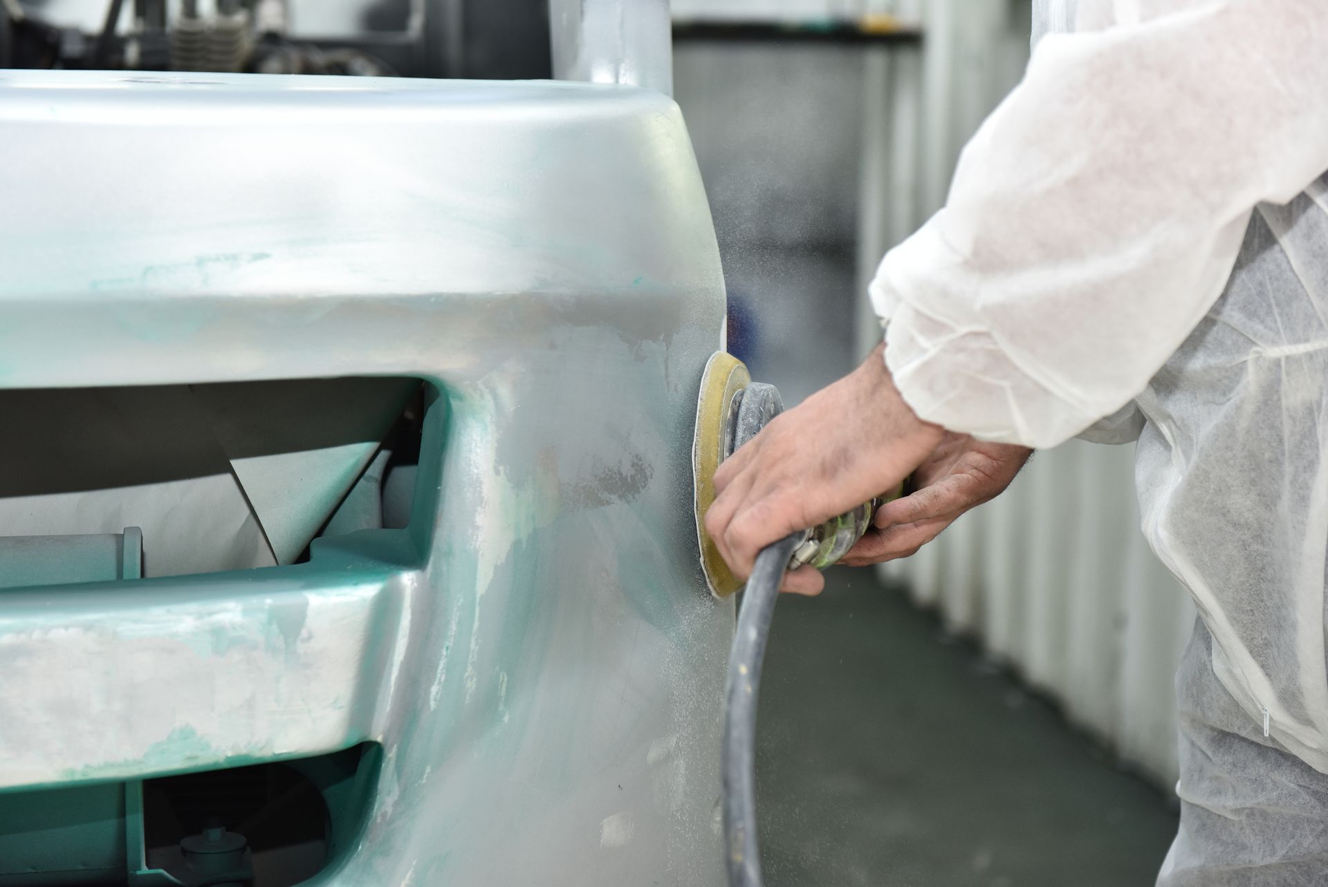 Worker sands car bumper to restore surface during auto body panel repair process.
