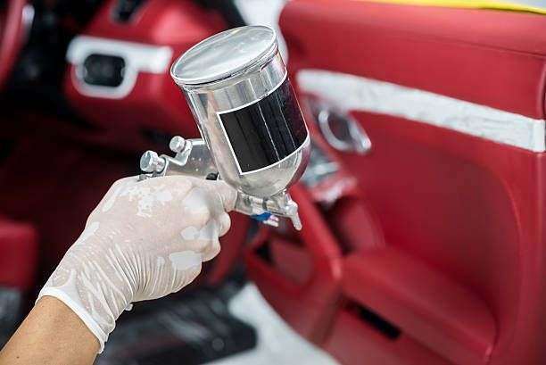 Close-up of hand holding car spray painter, with a blurry red car in the background.