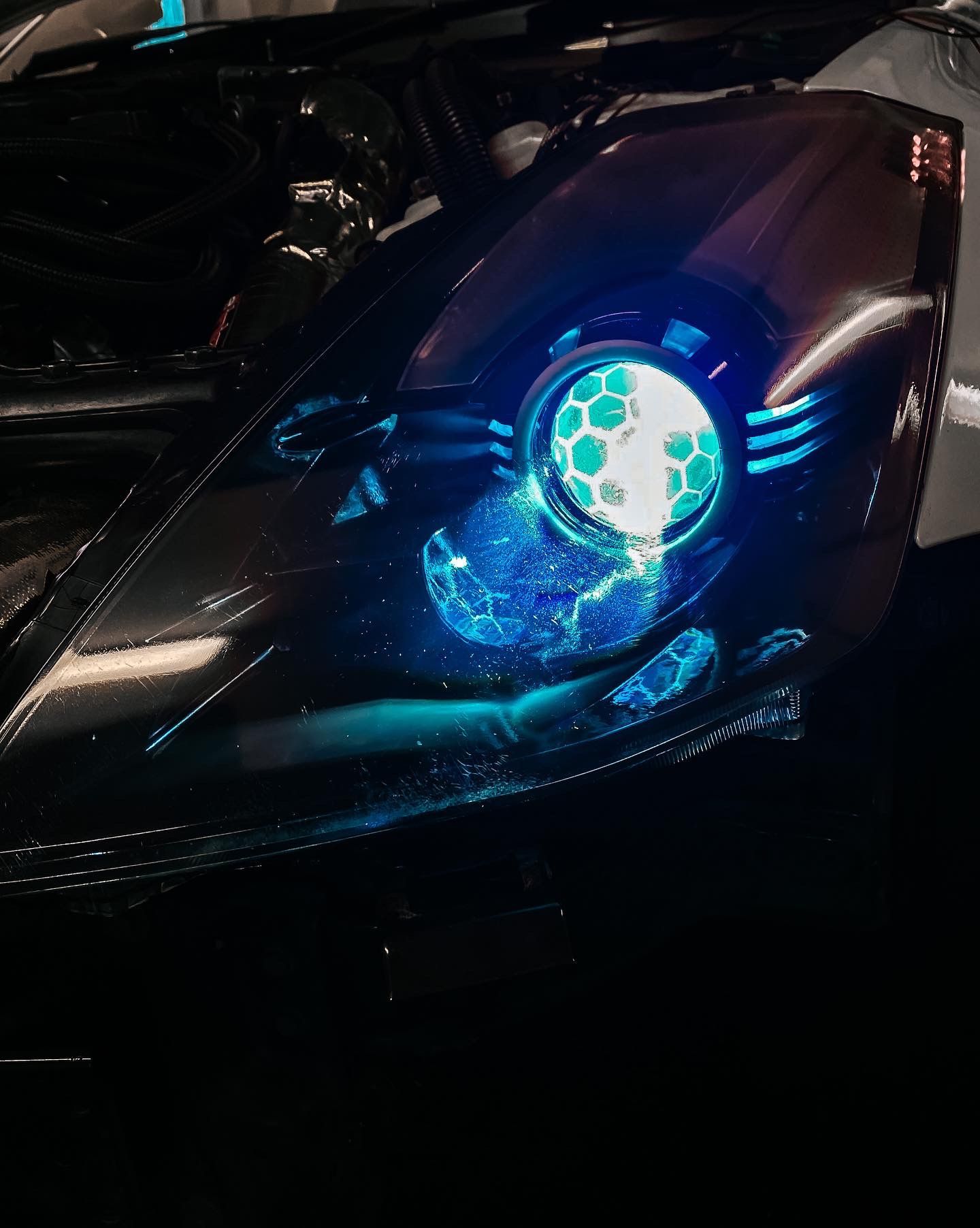 A car headlight glowing with a bright blue, honeycomb-patterned LED projection and electric lightning-like effects.