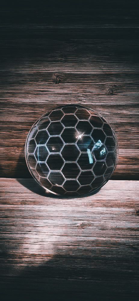A glass sphere with a dark honeycomb pattern resting on a weathered wooden surface.