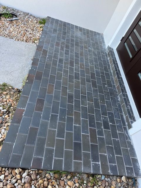 A brick walkway leading to a door with rocks on the ground