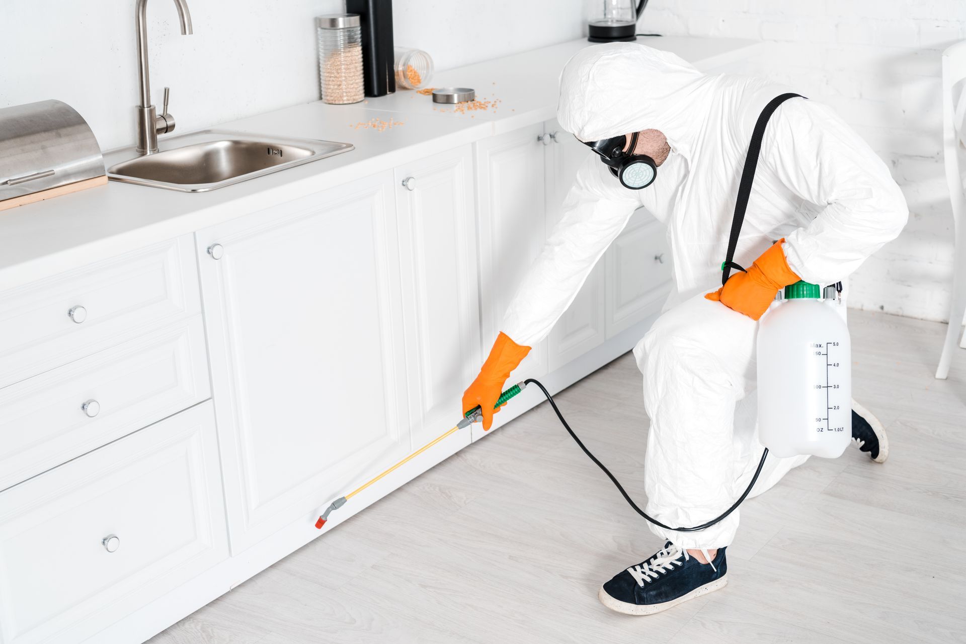 A man in a protective suit is spraying a kitchen with a sprayer.