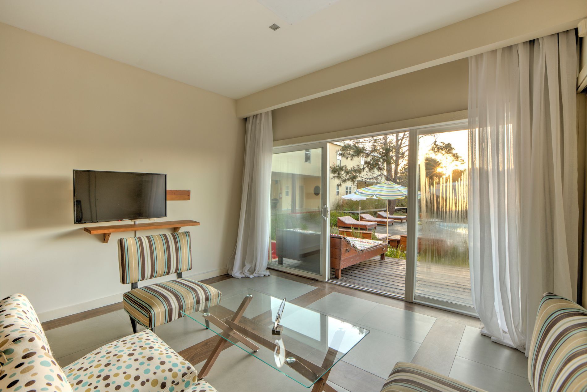 Una sala de estar con sofá, silla, mesa, televisión y puertas corredizas de vidrio.