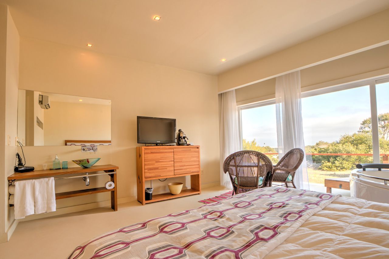 Una habitación de hotel con cama, sillas, televisión, espejo y puertas corredizas de cristal.