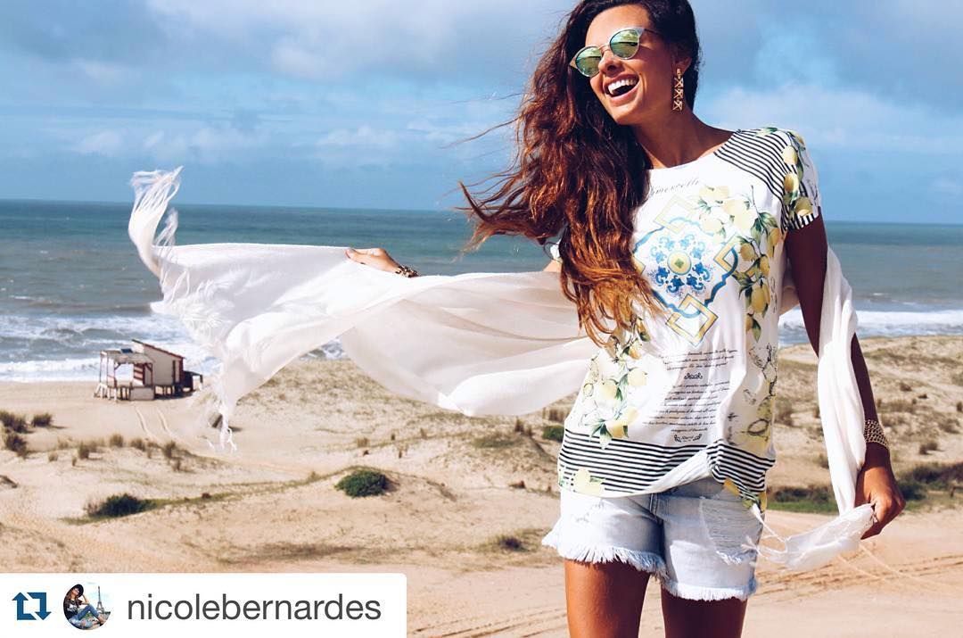 Una mujer está parada en una playa sosteniendo una bufanda blanca.