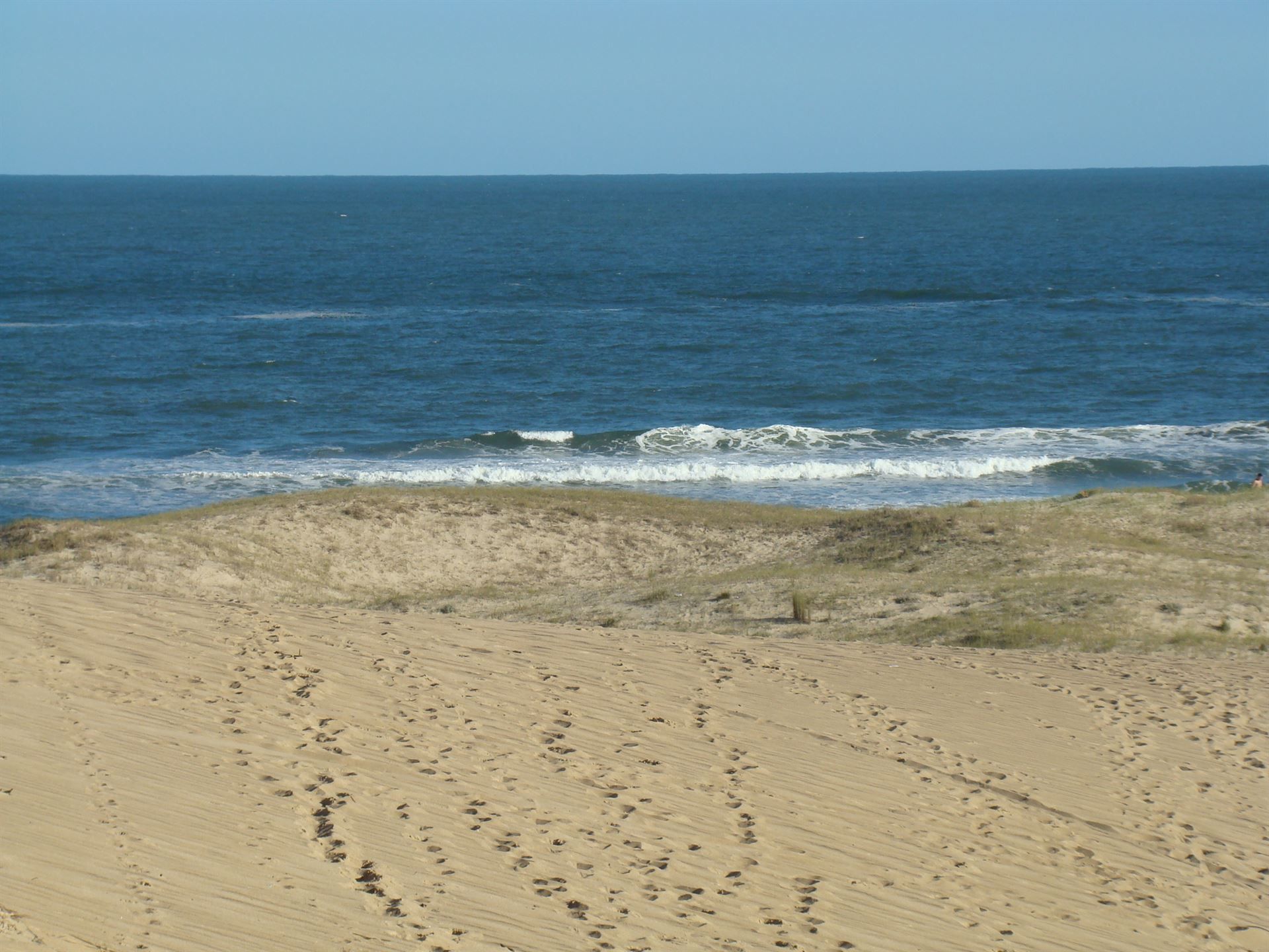 Una playa de arena con una gran masa de agua al fondo.