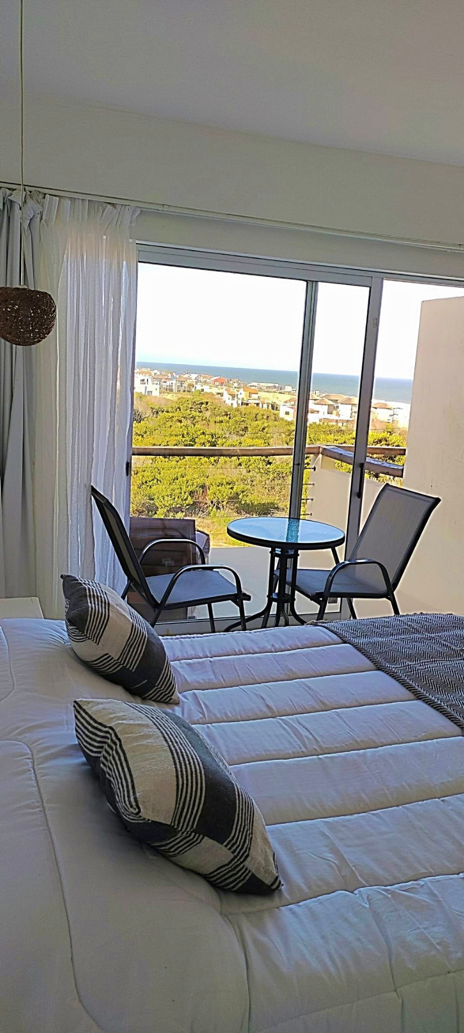 Un dormitorio con cama, sillas, mesas y vista al mar.