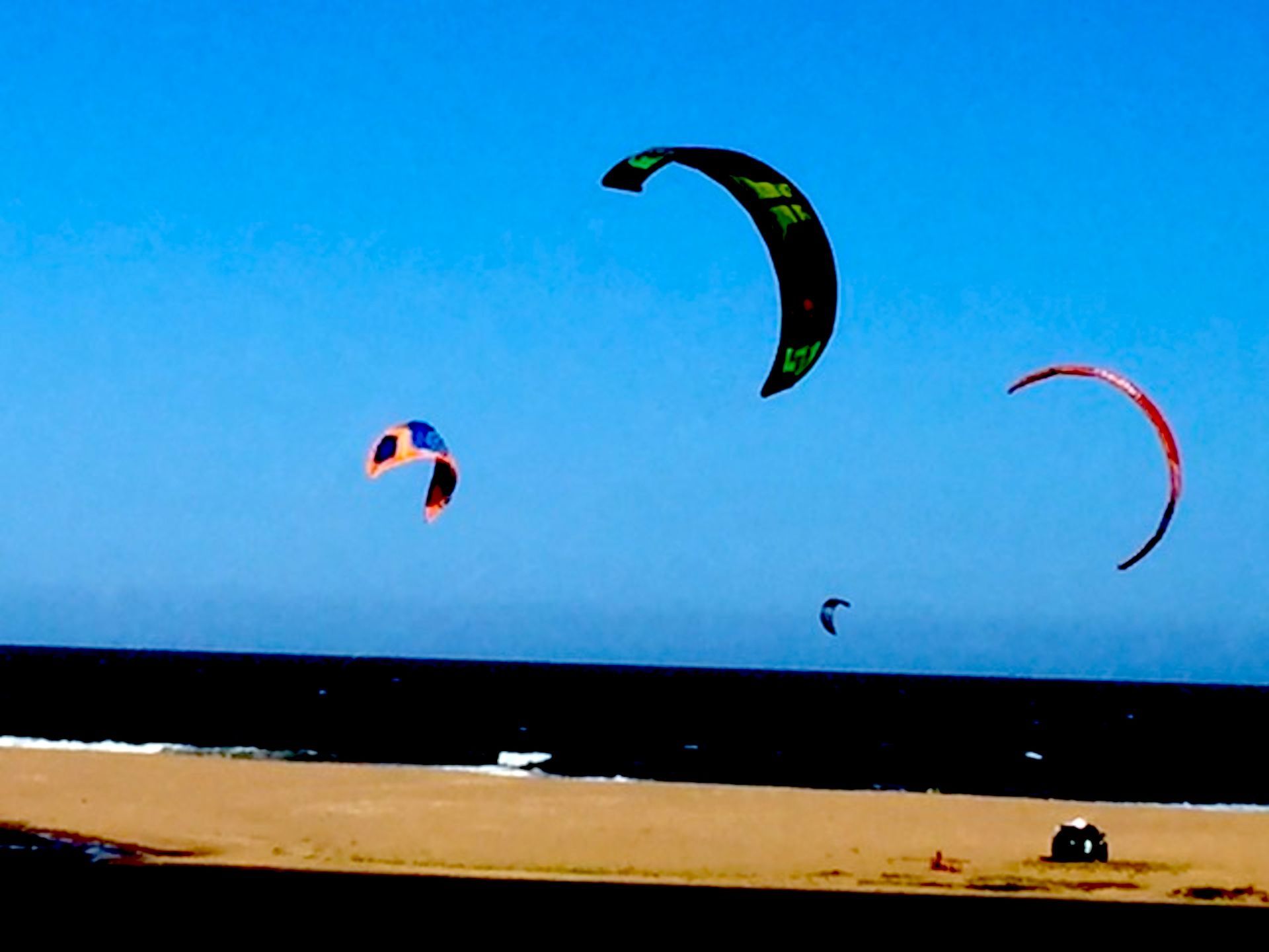 Tres cometas vuelan sobre una playa de arena