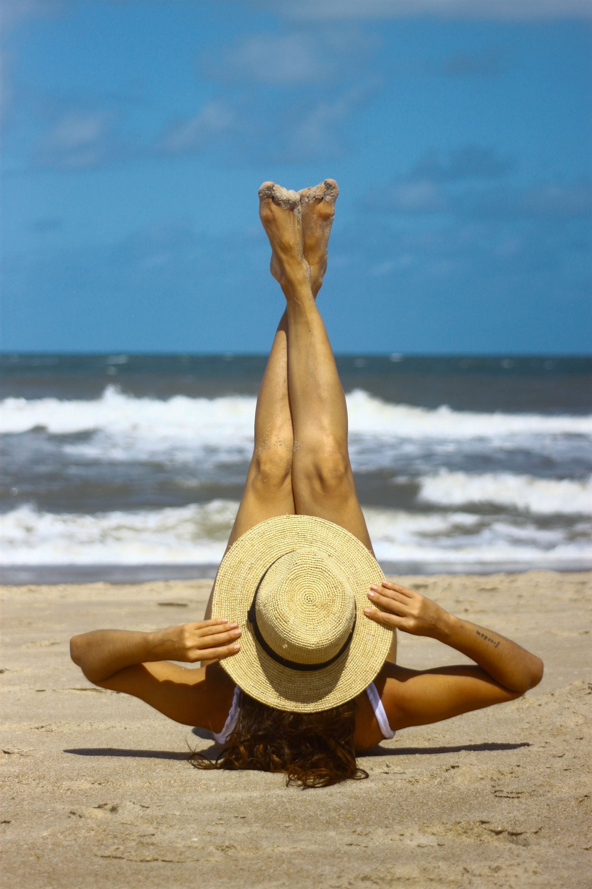Una mujer está acostada boca arriba en la playa con las piernas en el aire.